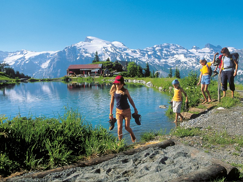 De kids wandelen met de ouders langs het meer met besneeuwde bergtoppen op de achtergrond