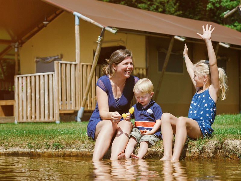 Een gezin zit lekker met de voetjes in het water op babyvriendelijk vakantiepark Dierenbos.