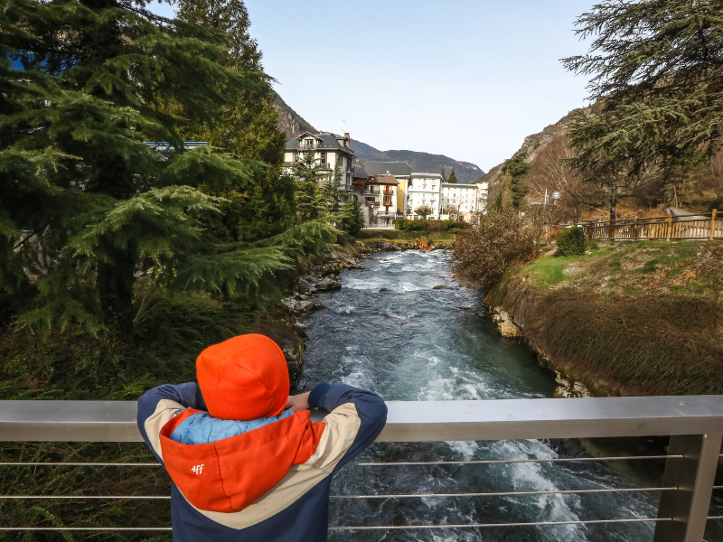 De zoon van Elisabeth kijkt over het water naar het Grande Hotels des Thermes in Brides-les-Bains, Franse Alpen