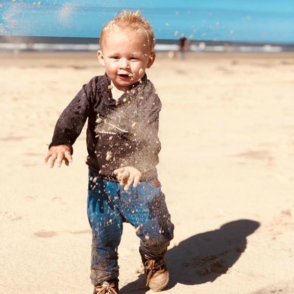 Jongetje met opspattend zand op het strand in Egmond aan zee