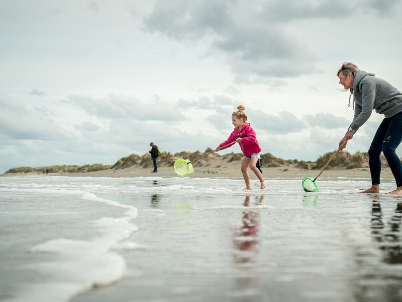 Gezin op het strand met schepnetjes vissen in de zee