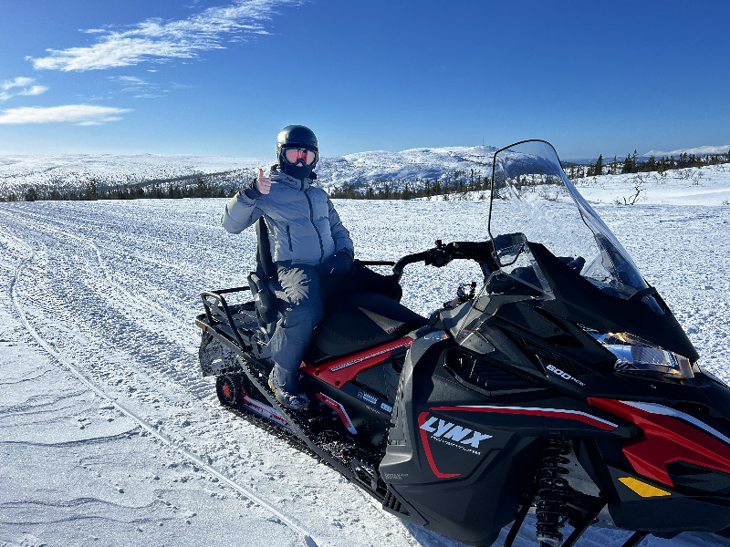 Lara zit achterop de sneeuwscooter. Wat opvalt is de goede rugleuning 