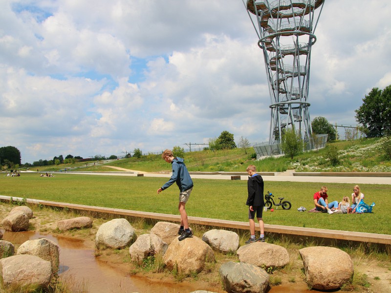 De jongens klauteren over de stenen in het Spoorpark. Op de achtergrond zie je de uitkijktoren.