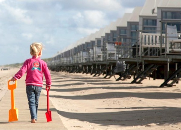 Strandvakantie in Nederland, meisje loopt met schep langs de strandhuisjes