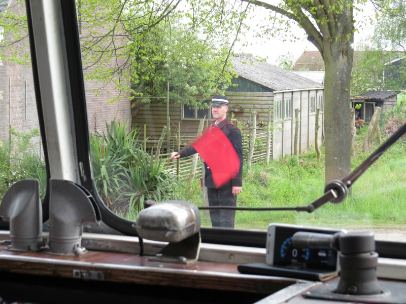 De conducteur zwaait met zijn vlag bij een spoorwegovergang