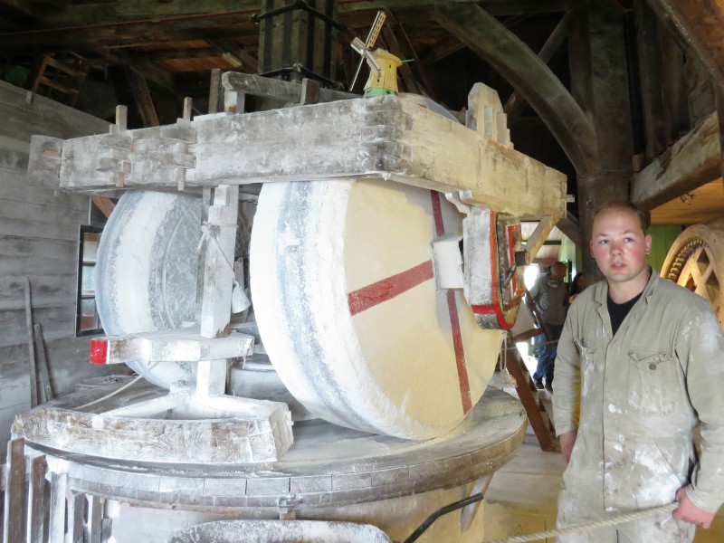 De molenaar bij de grote draaiende molenstenen van verfmolen de Kat