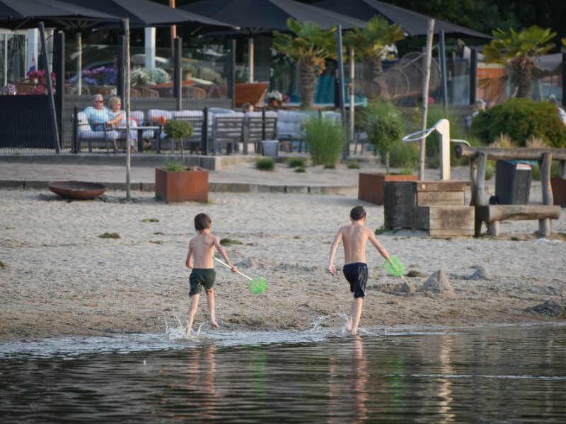 De kinderen zijn lekker aan het spelen aan de waterkant en vader en moeder kunnen relaxen op het terras