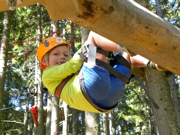 Jongen in het klimpark hangend aan de zijkant van een boomstam