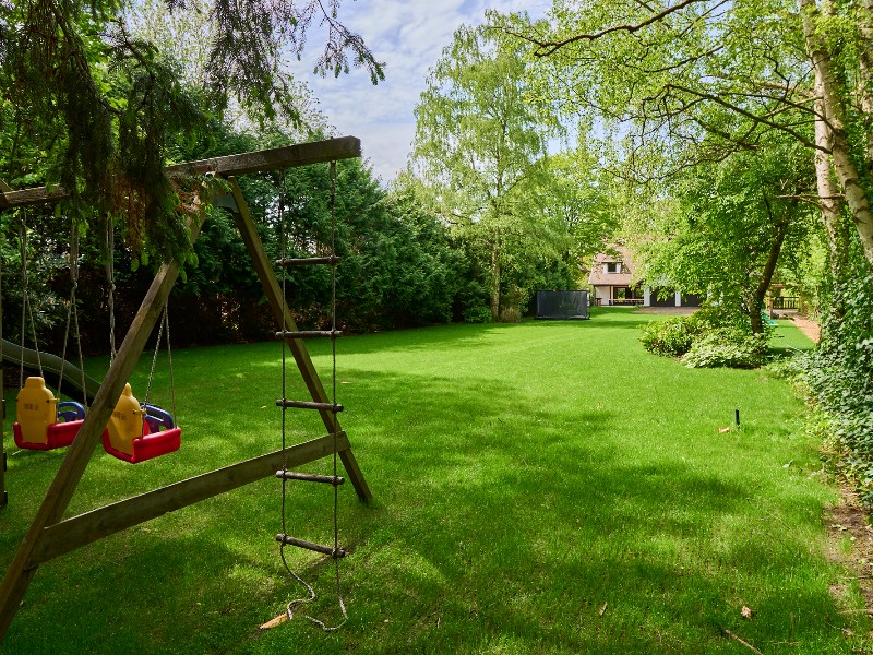 Uitzicht op de achterkant van Villa Bosrijk vanuit de tuin en schommel