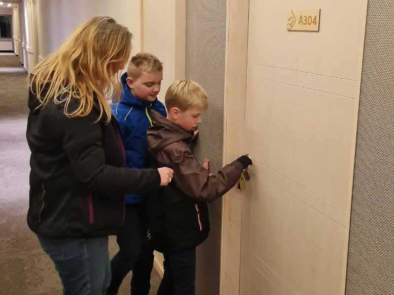 Alma staat voor de deur van de familiekamer met haar kinderen