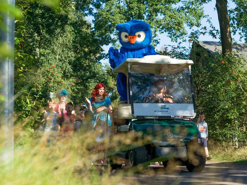 De mascotte Cobus rijdt over de camping